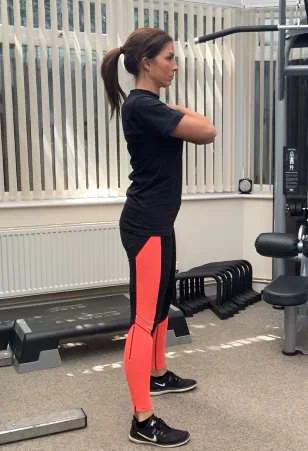 Beginning of the squat exercise, standing with arms crossed over chest.