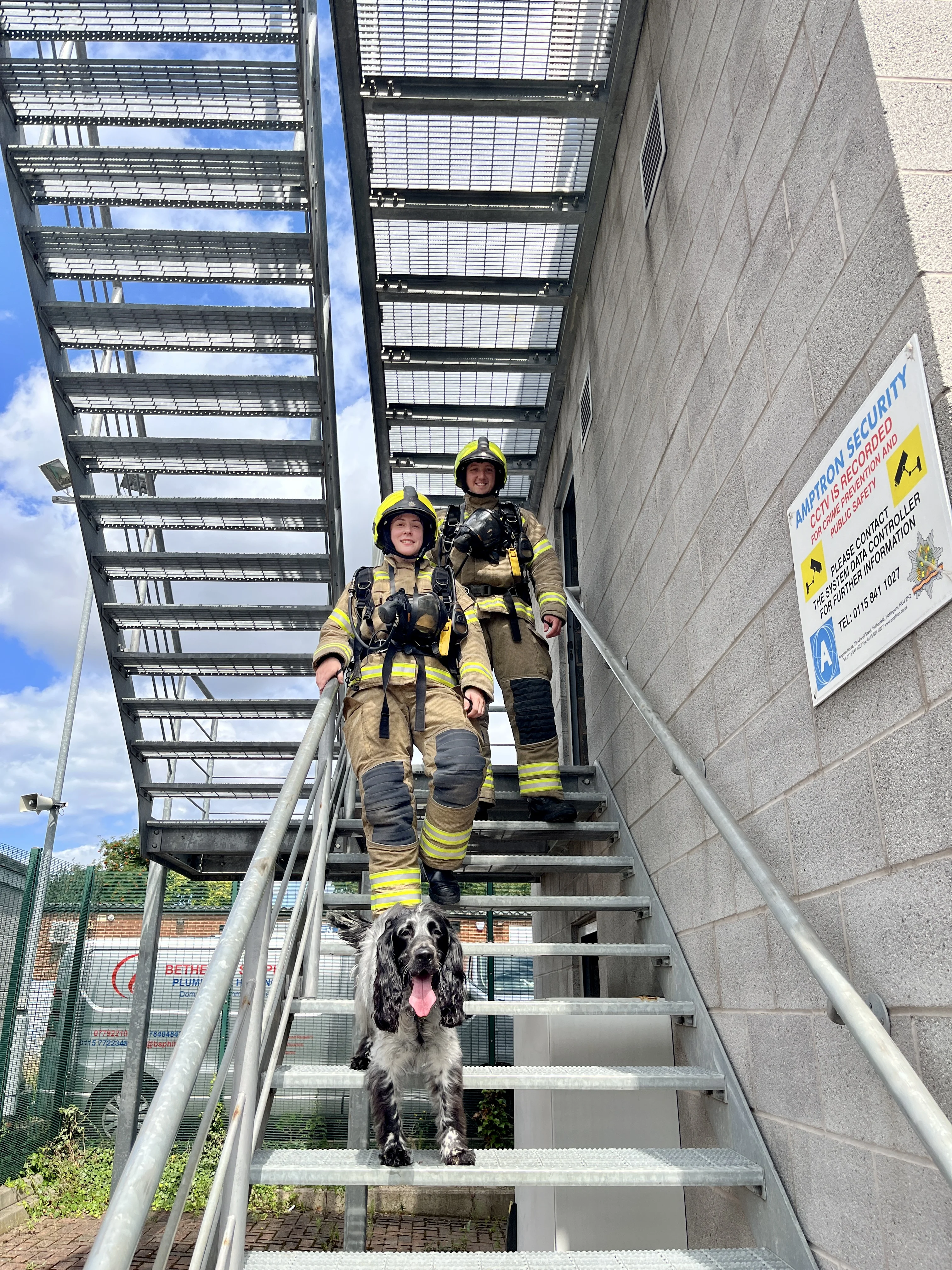 Male and Female firefighter walking down the stairs of carlton fire station smoke house in fire kit with the fire dog