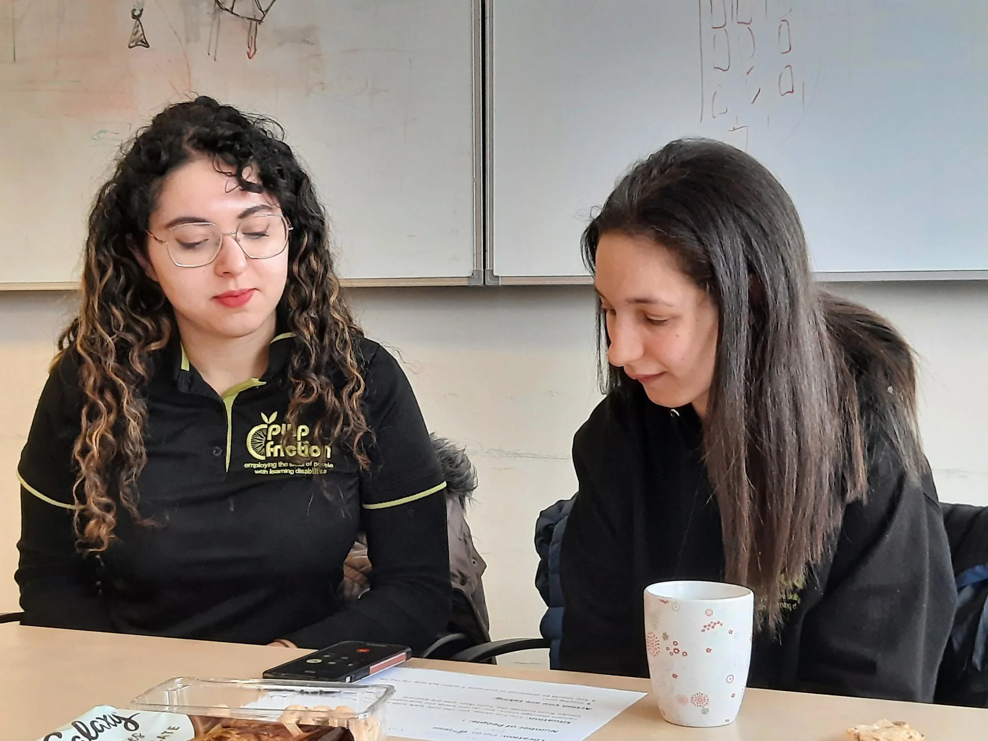 two young women look down at a piece of paper on a table