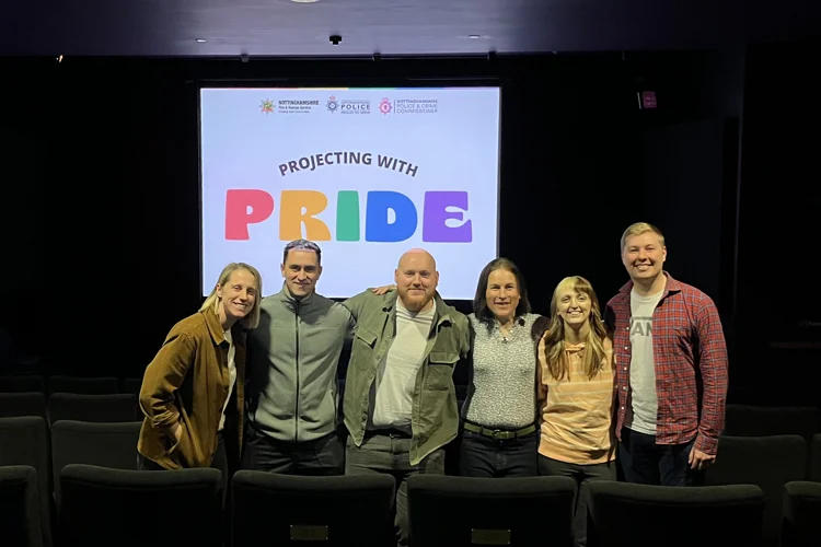 Event organisers stand amongst the cinema seats with 'Projecting with Pride' logo on a screen behind them.