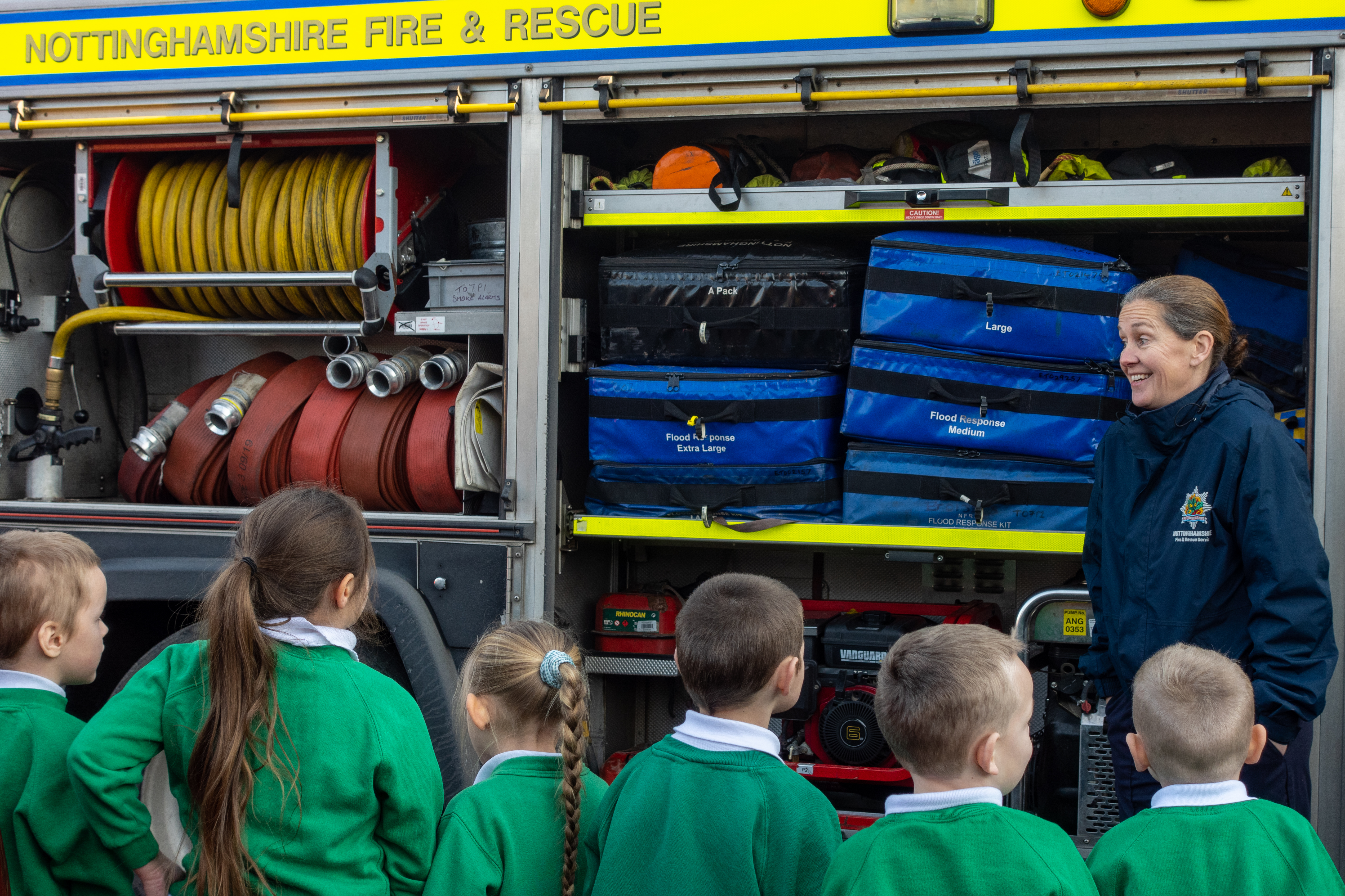 Schoolchildren lined up listening to a firefighter explain about her role.