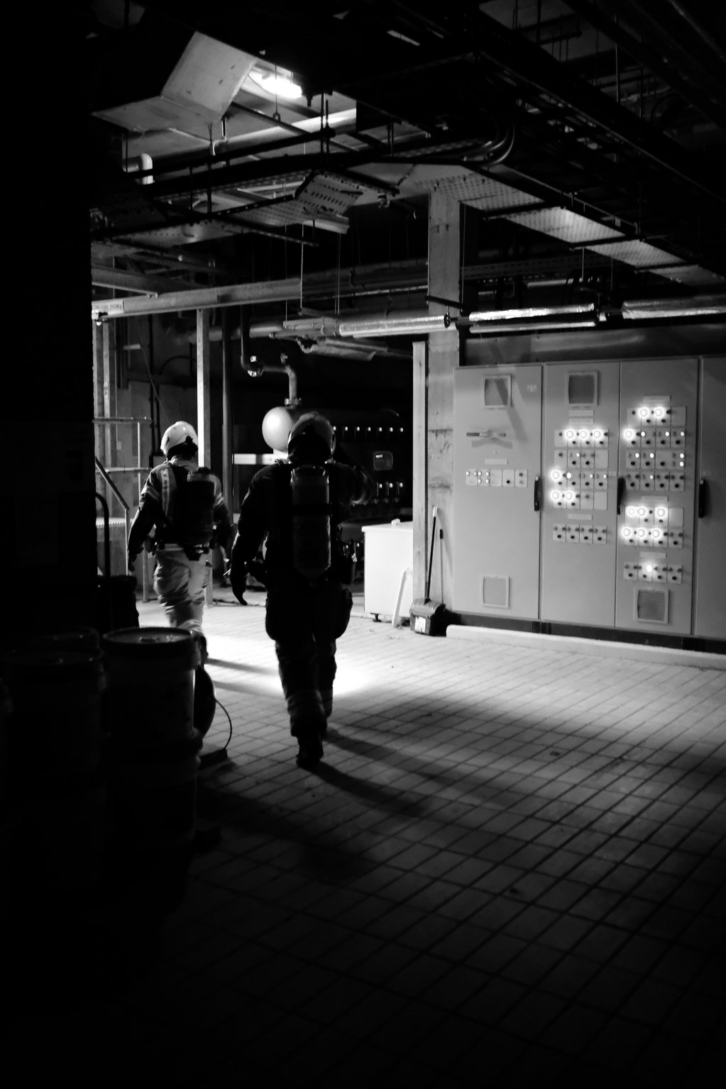 Black and white image of two firefighters walking out of a plant room.