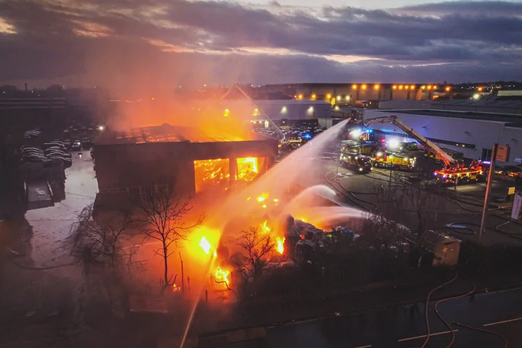 A fire in an industrial building with water jets spraying the fire and fire engines visible around the outside.