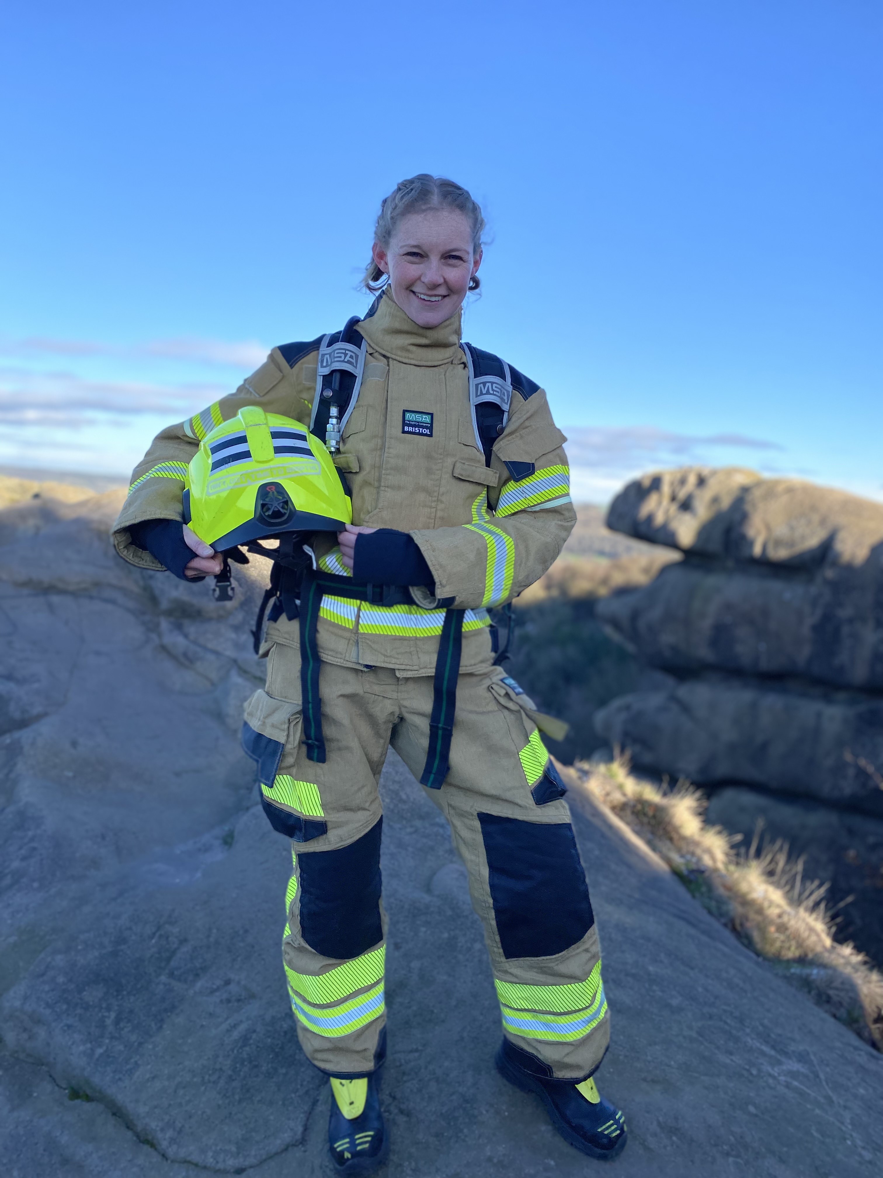 Firefighter Needham in fire kit holding helmet smiling