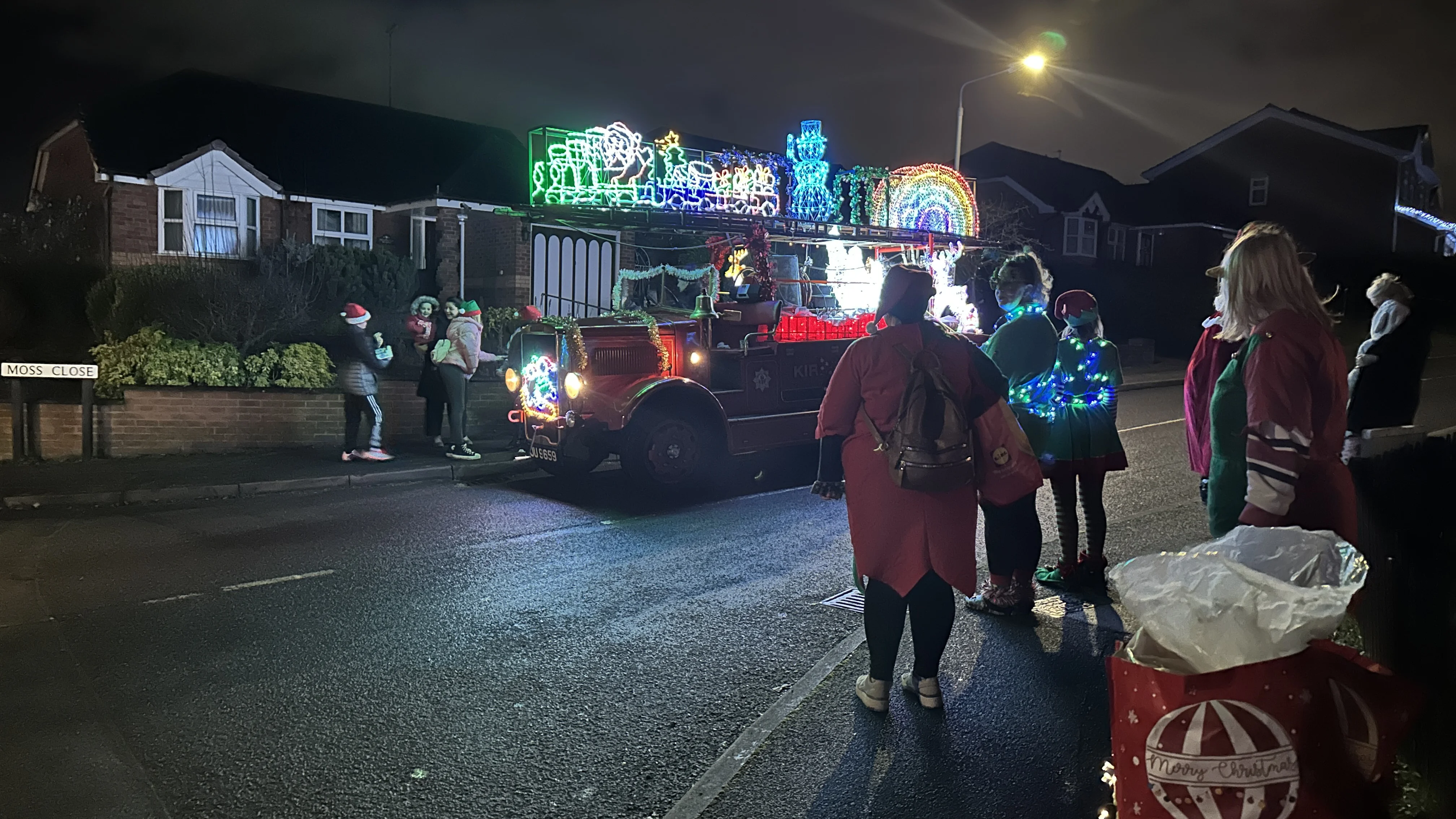 vintage fire engine with christmas lights parks outside a residential house, people are crowded around it
