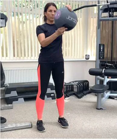 A women holding a medicine ball at shoulder height and rotating it