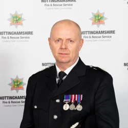 Mick Sharman in formal uniform standing infant of the Nottinghamshire Fire and Rescue Service badge.