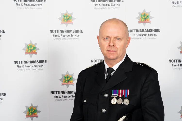 Mick Sharman in formal uniform standing infant of the Nottinghamshire Fire and Rescue Service badge.