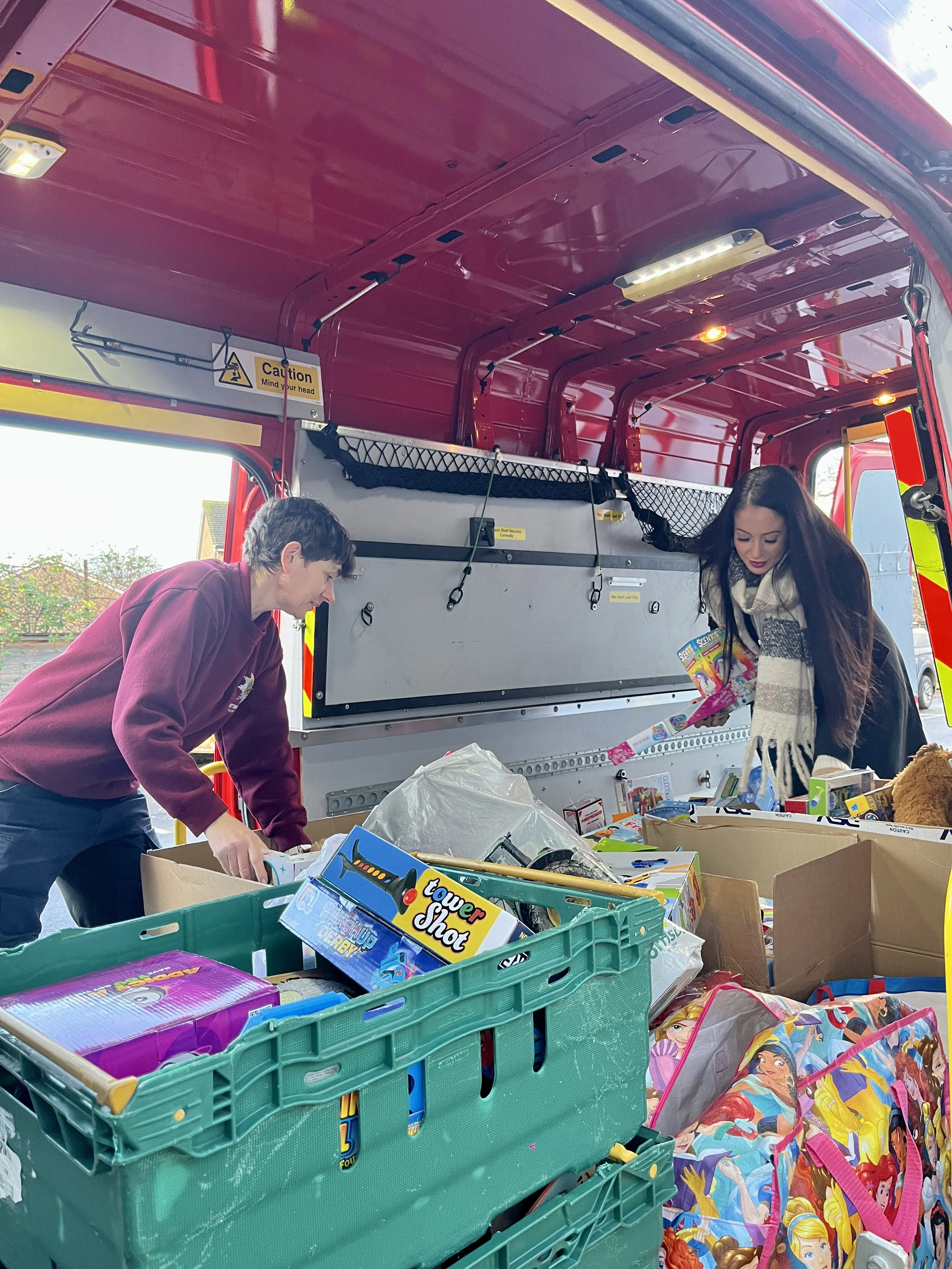 two people stand inside a van sorting boxes and crates of children's toys