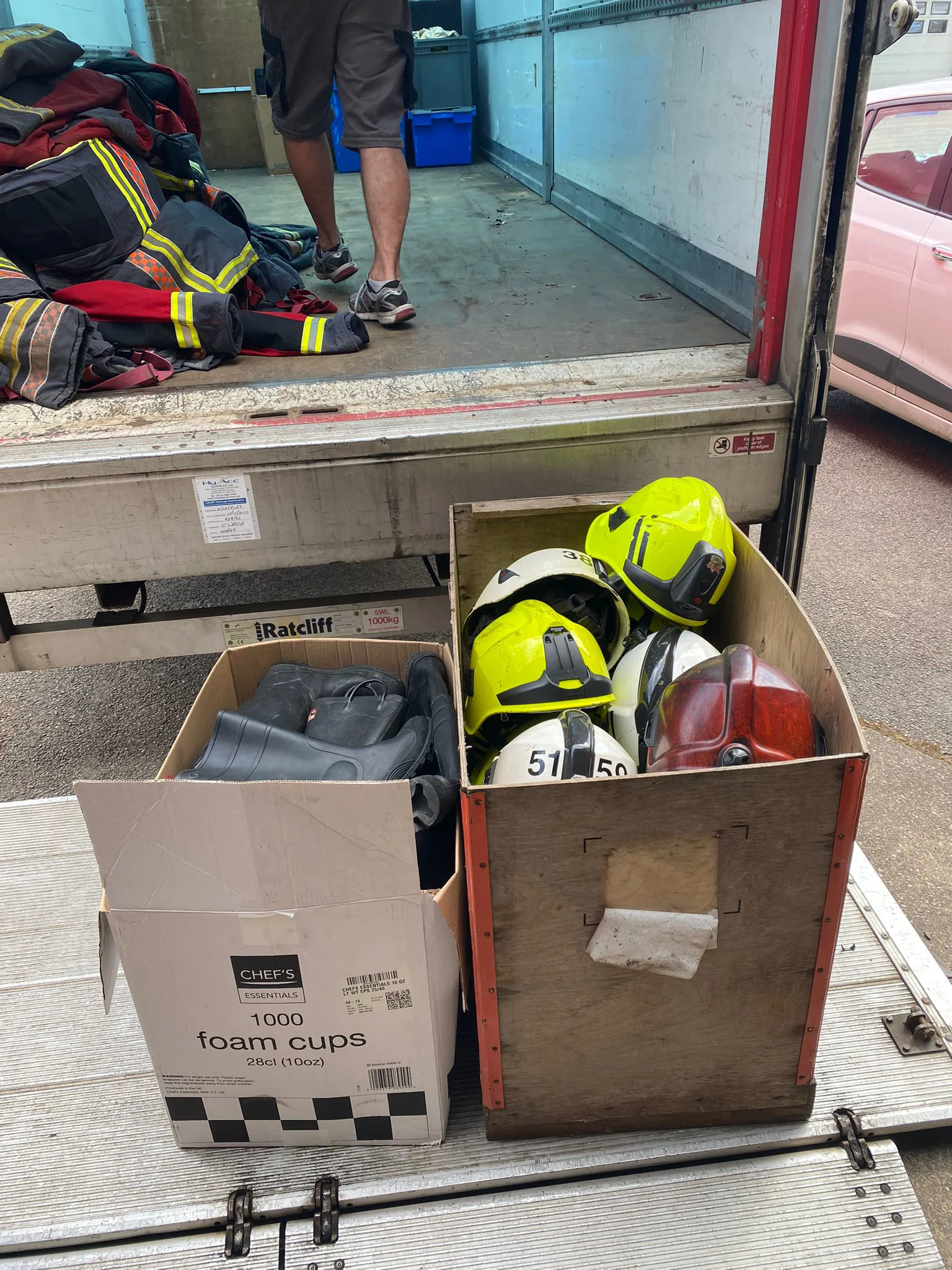 photo of the back of a lorry, two cardboard boxes hold boots and helmets