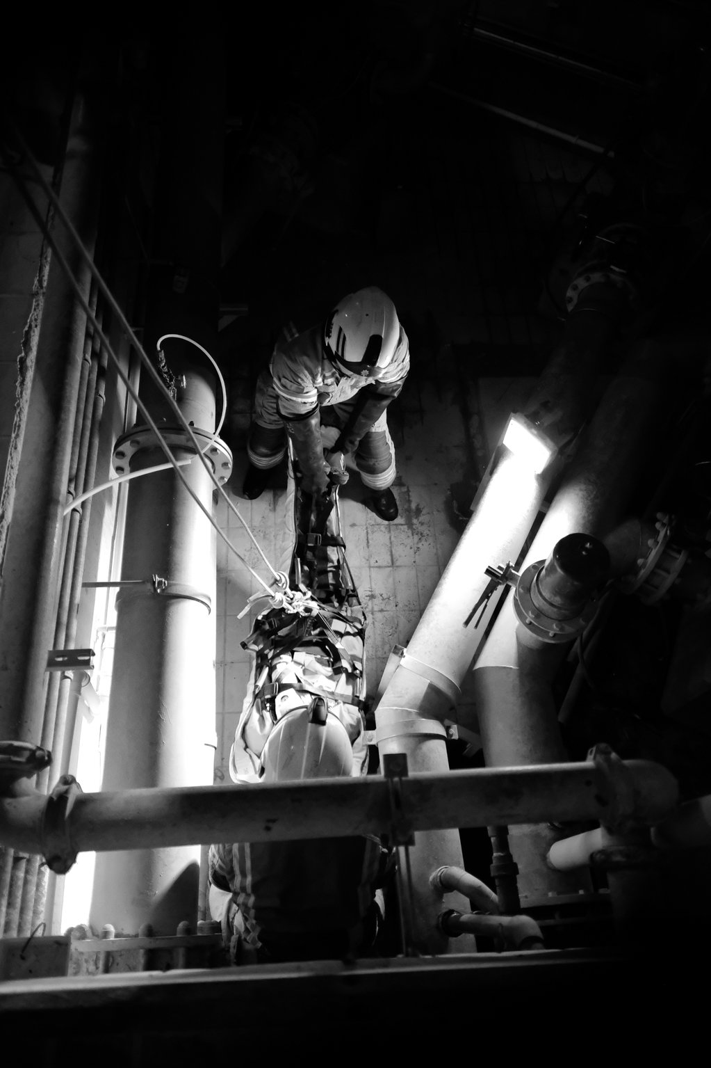 Black and white image of two firefighters lifting a dummy casualty in a stretcher.