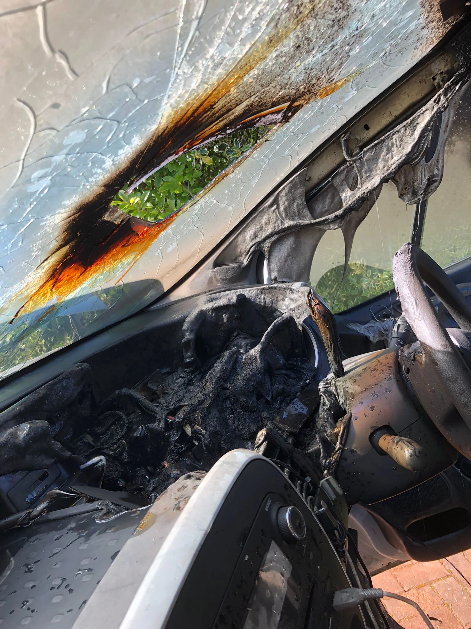 The burnt out inside of a car with hole in the windscreen where sunlight has been refracted