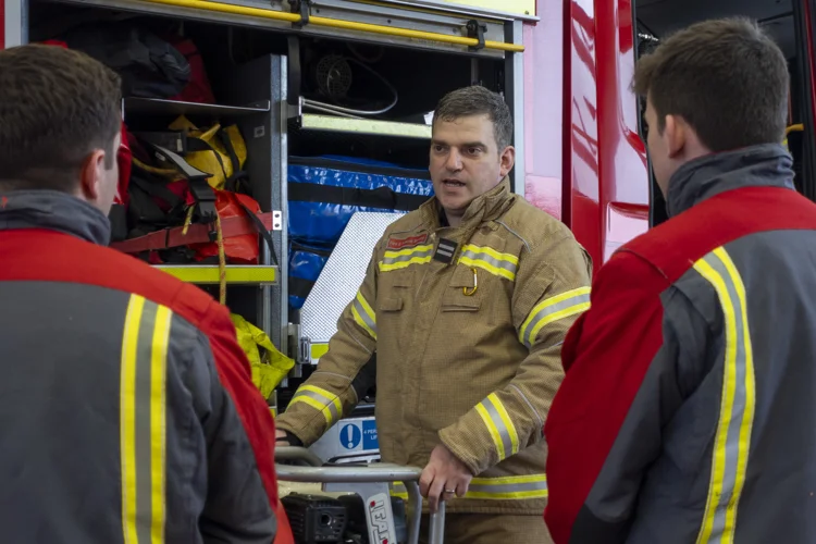 A firefighter speaks to soldiers while opening the fire engine locker.