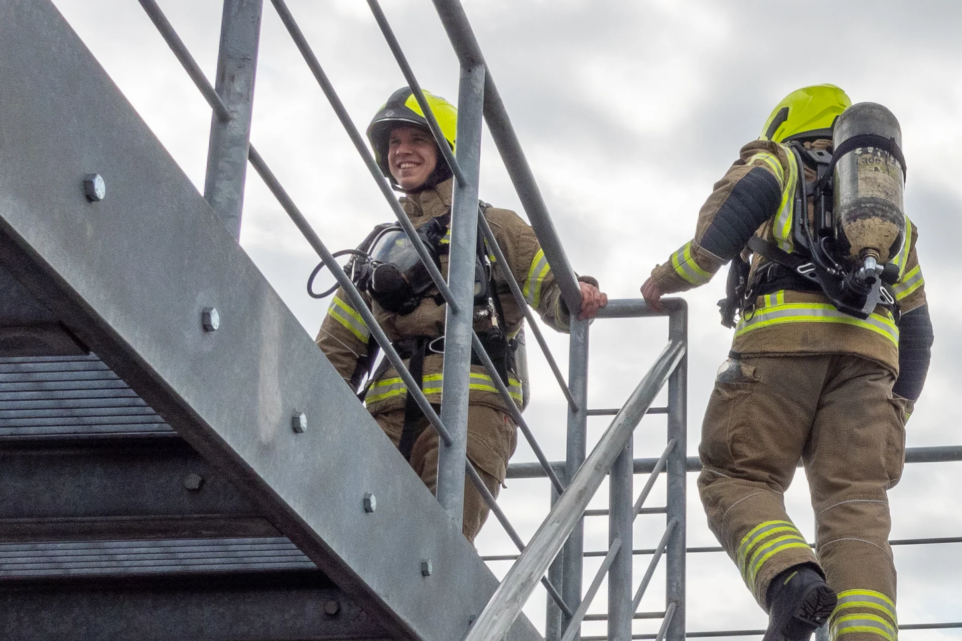 Two firefighters walking up some stairs in fire kit and BA