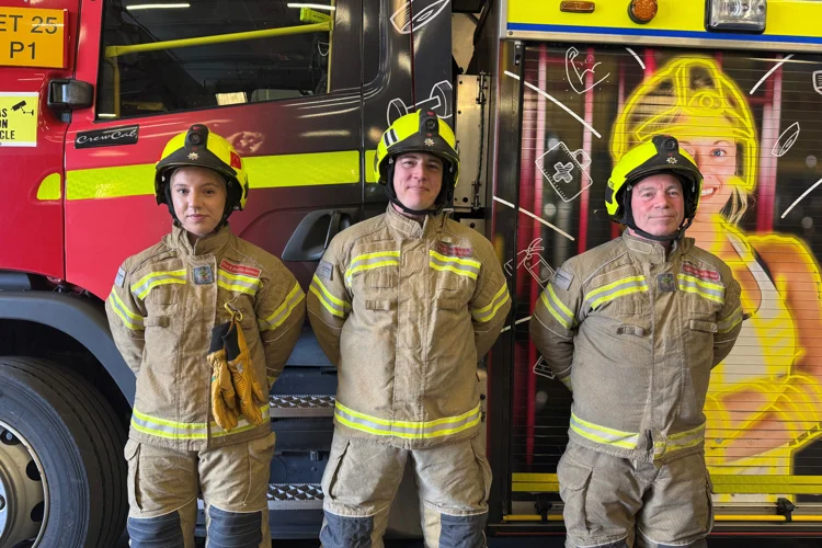 Three firefighters in fire kit including helmets at the side of the fire engine