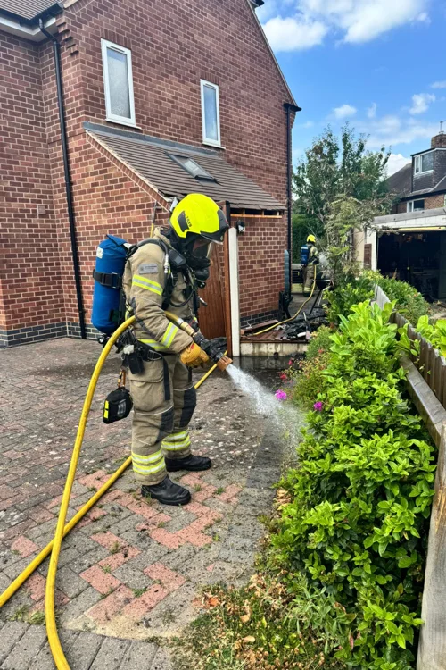 Firefighter in kit using a hose to put out fire in bush