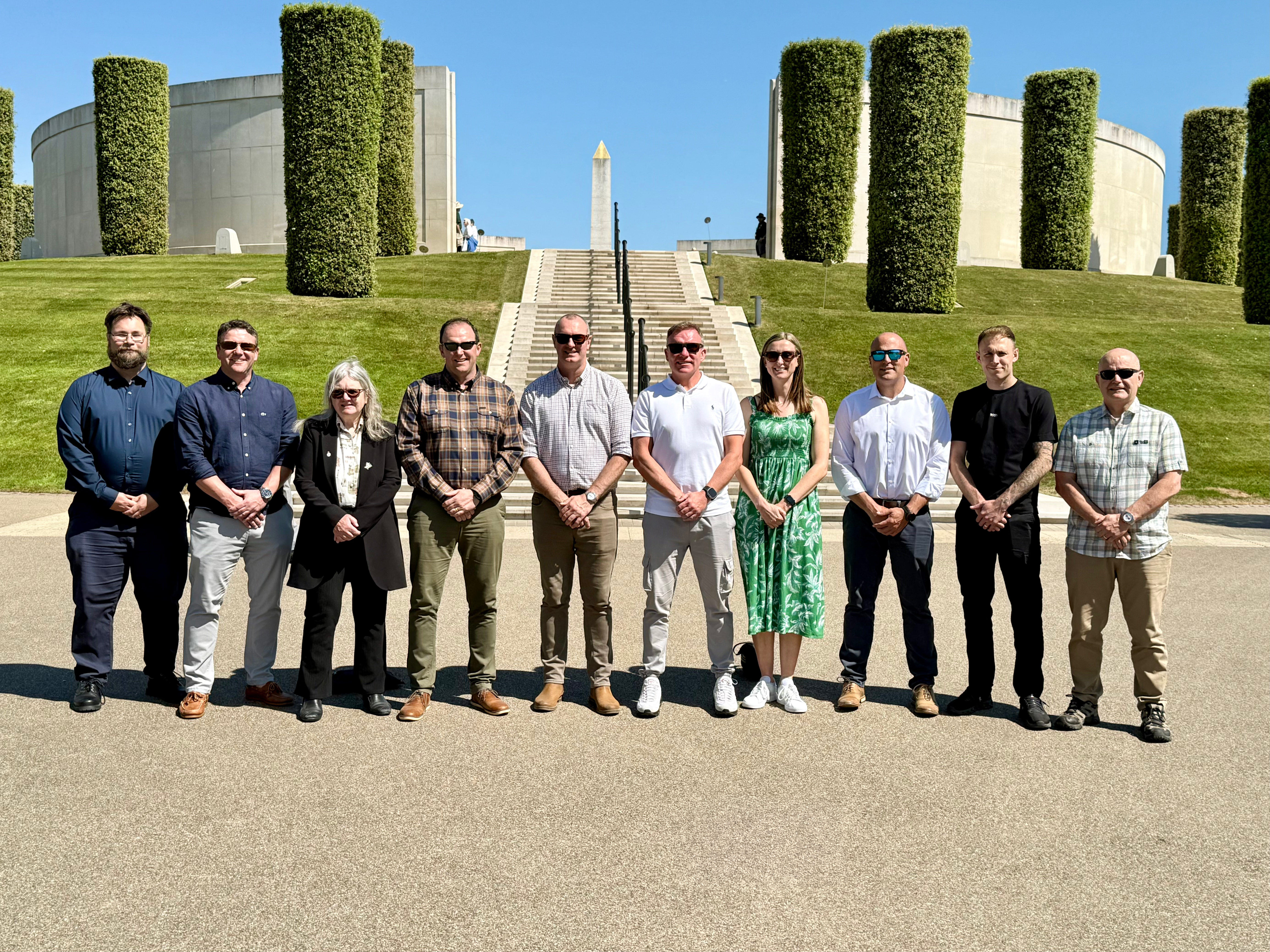 10 members of the Armed Forces Network standing in front of the Armed Forces Memorial at the National Memorial Arboretum