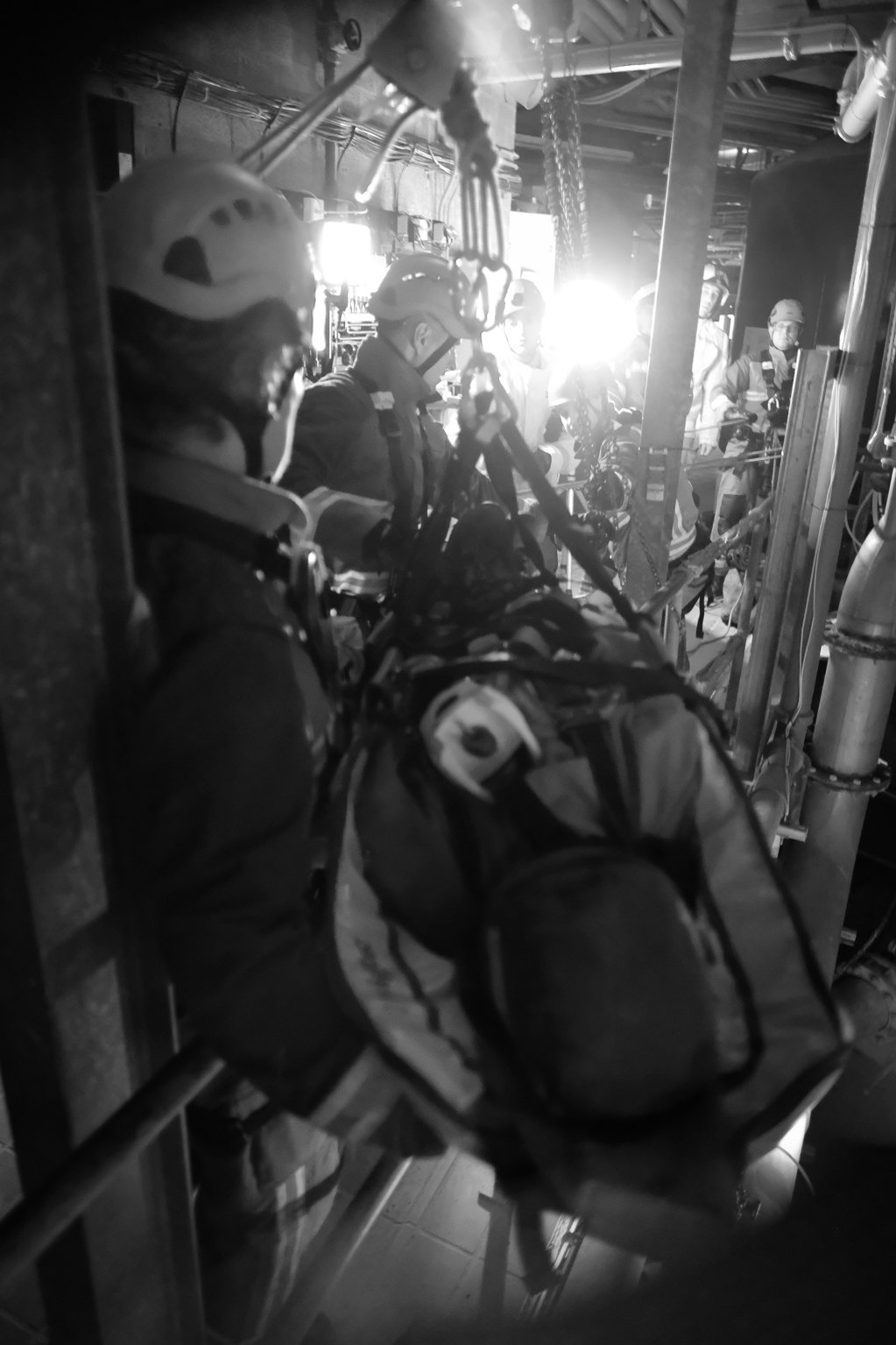 Black and white image of a dummy casualty being rescued by firefighters after its been lifted up in a stretcher.