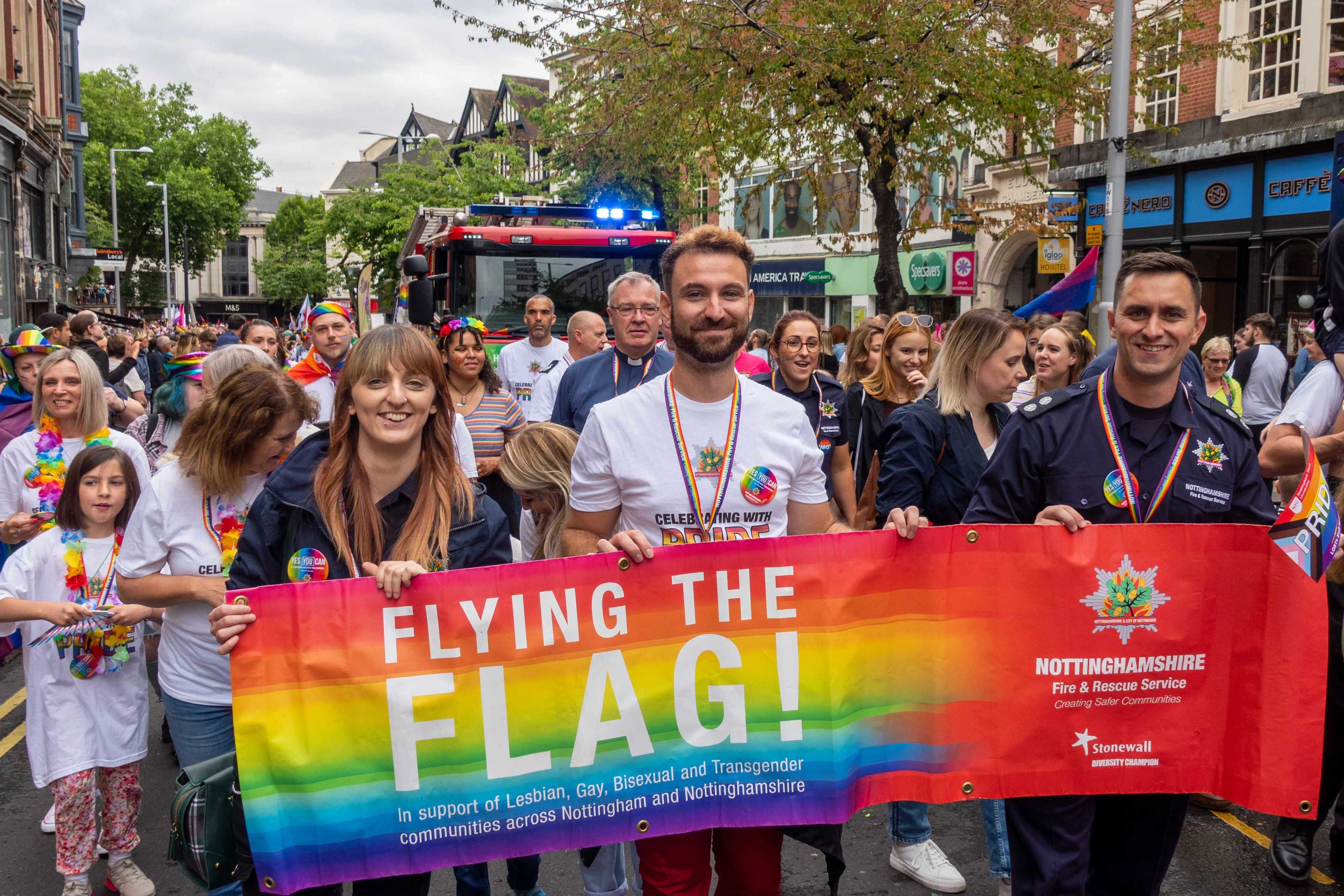 Nottinghamshire Fire and Rescue Service staff taking part in Nottingham Pride parade holding a large flag in rainbow colours