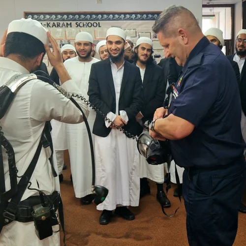A firefighter showing a group of students at a muslim school the breathing apparatus they wear.