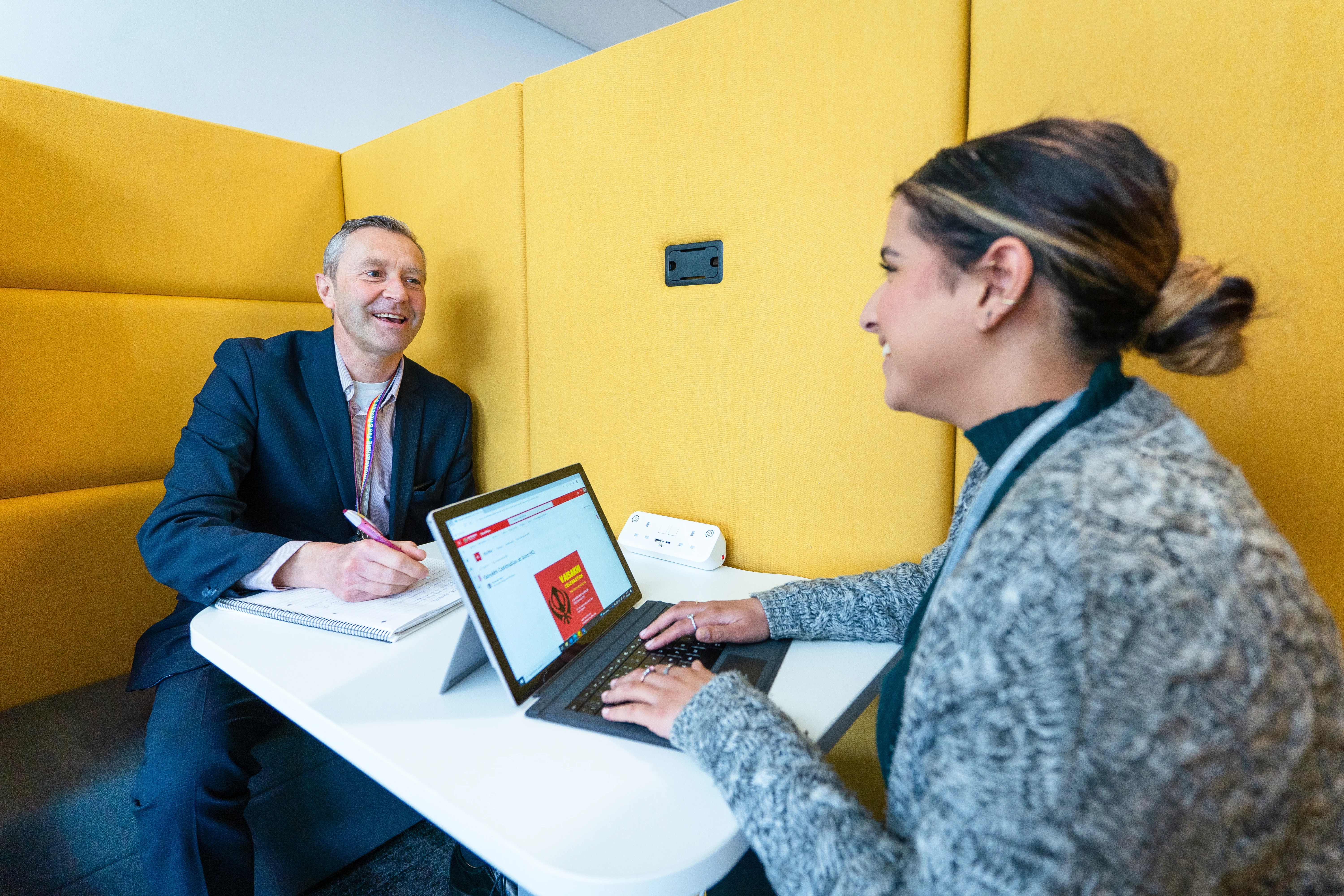 Two members of HR sit down smiling with laptop