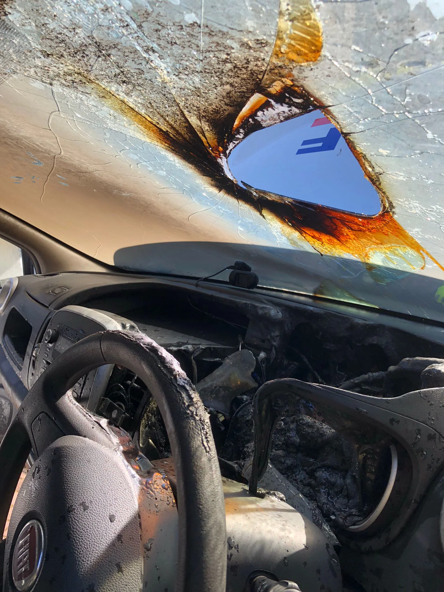 The burnt out inside of a car with hole in the windscreen where sunlight has been refracted
