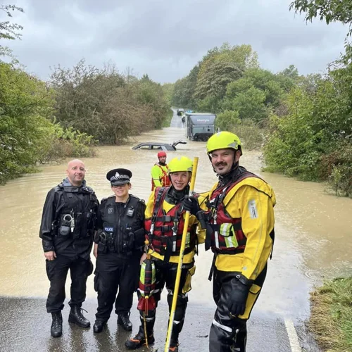 Police and Fire staff near a flooded road in Ashfield. A car and lorry stuck in the water behind.