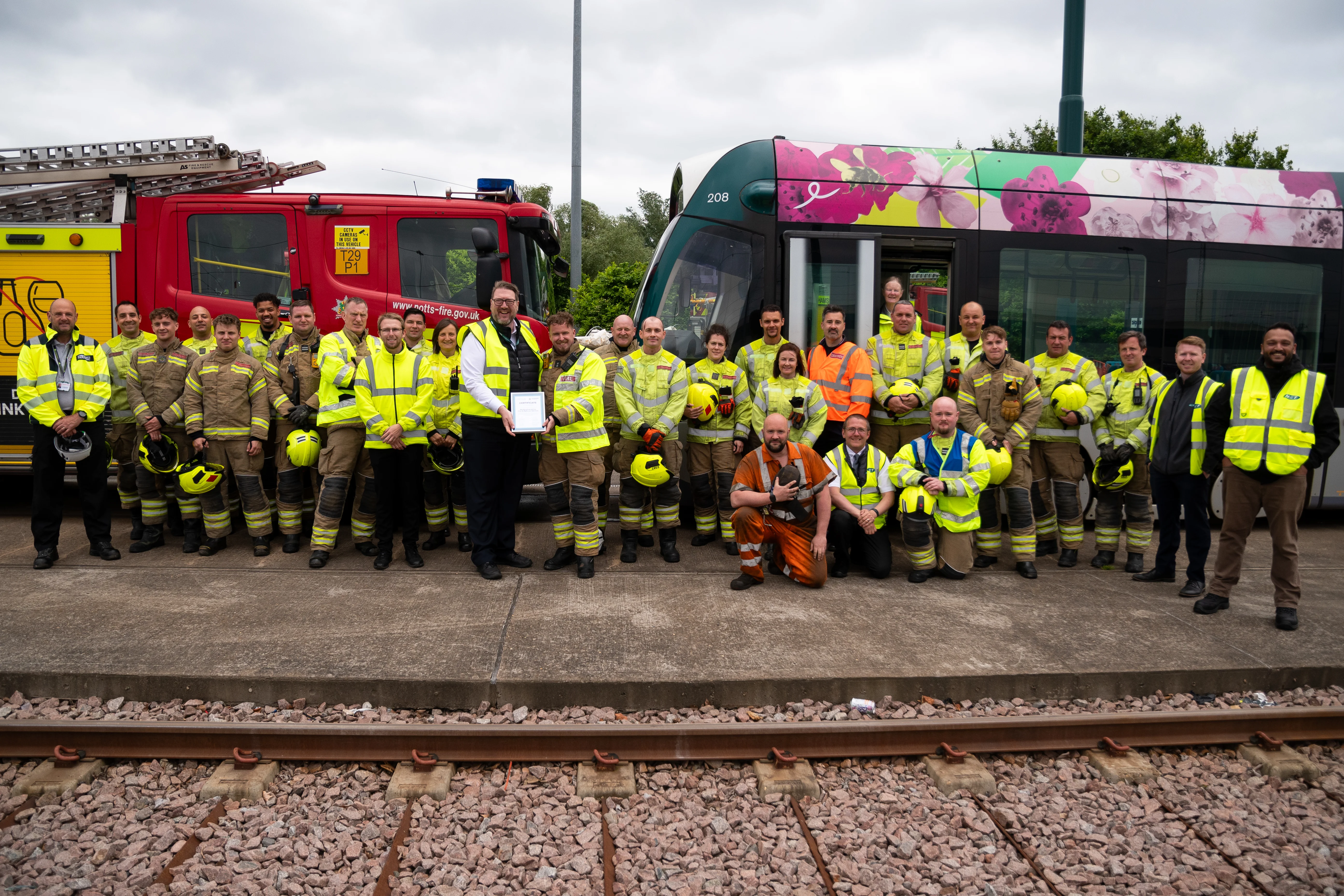 a group of people stand in front of a tram and fire engine