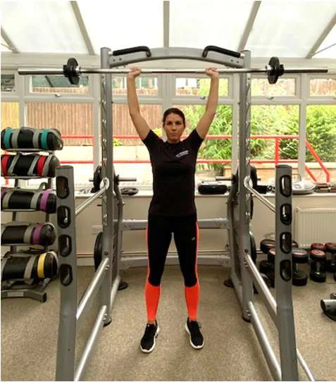 An overhead press in the lifted position, using a bar bell with weights on.