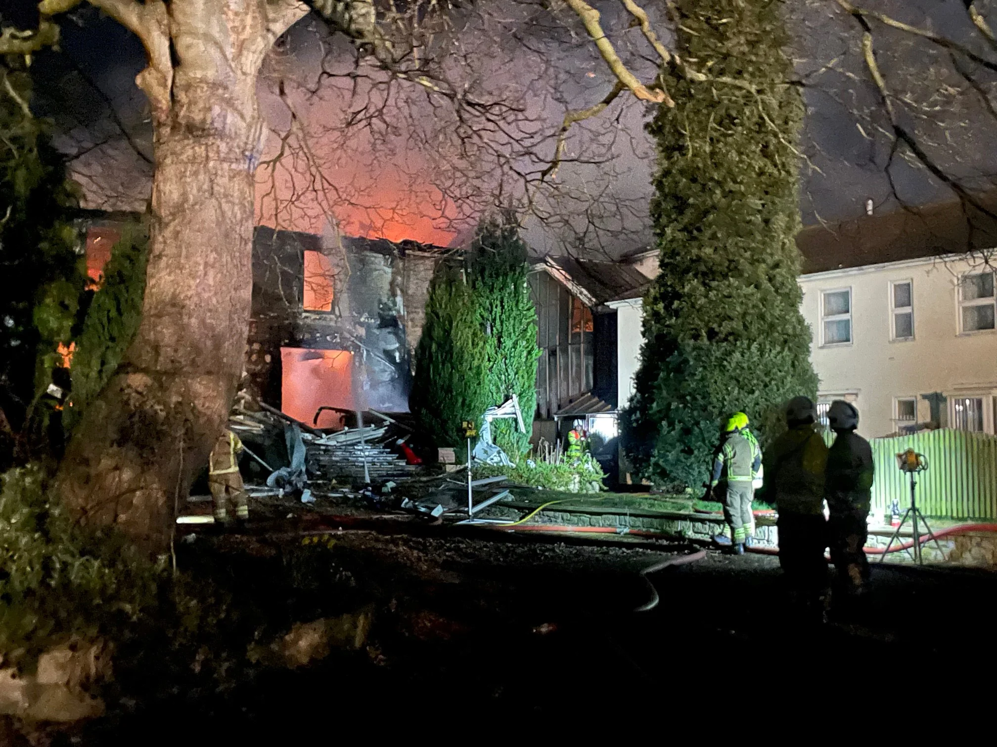 An orange glow and smoke can be seen from a derelict building with firefighters in the foreground