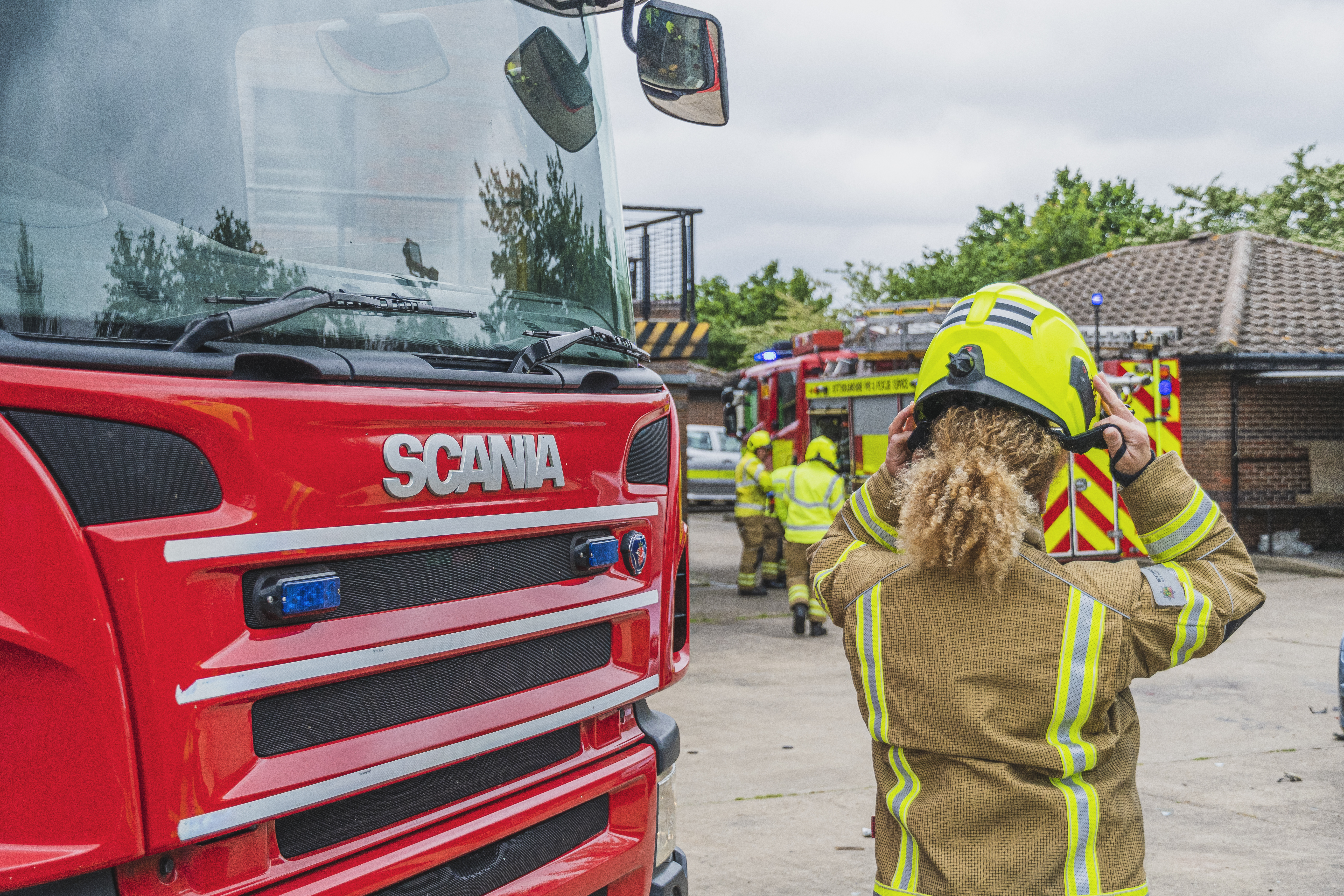 Female firefighter putting on a helmet infront of a fire engine.