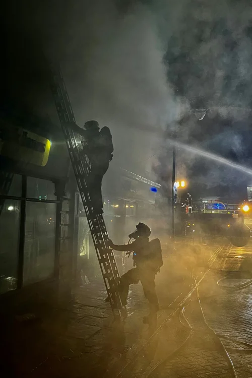 A firefighter climbs a ladder with smoke in the background.