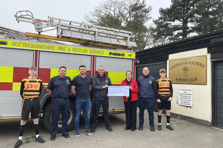 Firefighters and footballers from Collingham standing infront of fire engine holding big cheque