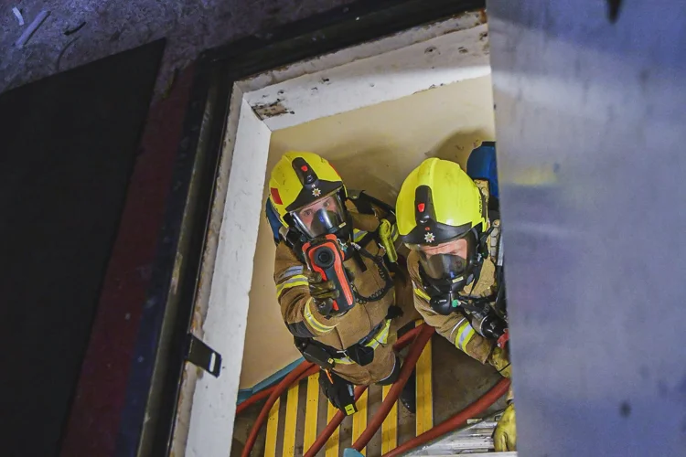 Two firefighters climbing a ladder into a loft using a thermal imaging camera