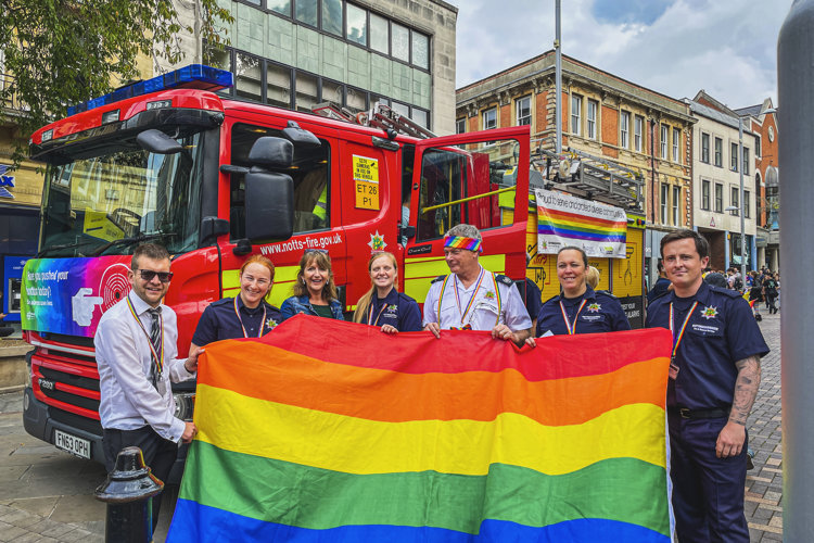 Group of seven fire service personnel holding a large rainbow flag at Nottingham Pride