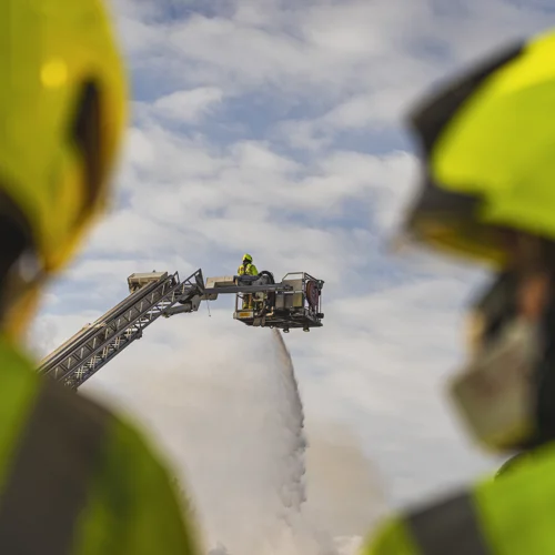 Two firefighters with an aerial ladder platform in the background.